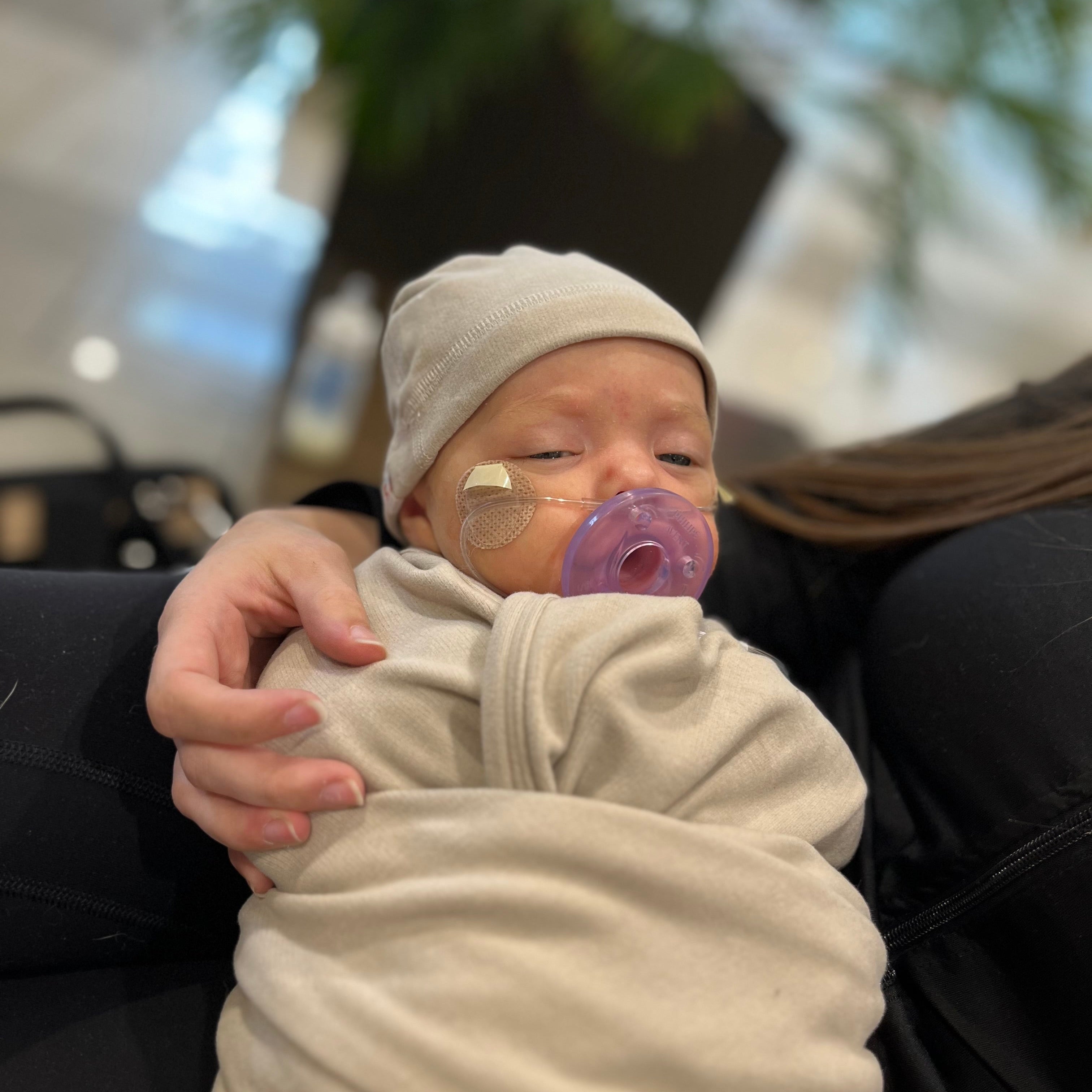 Newborn baby wrapped in a Wonder by Lurepa blanket with a pacifier, held by an adult in an indoor setting.