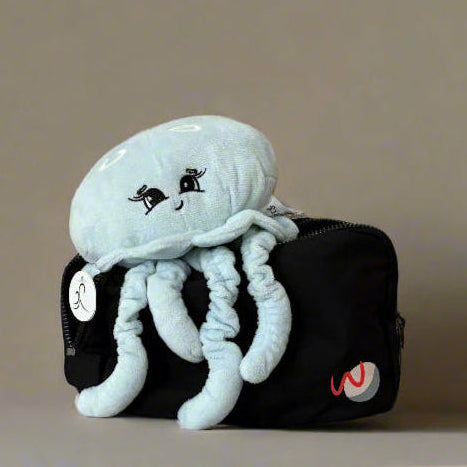 Plush jellyfish toy un a black pouch with a logo against a beige background