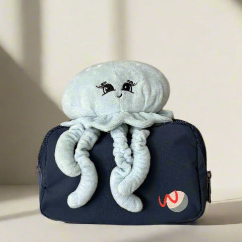 Plush jellyfish toy on a navy blue pouch with a logo against a neutral background