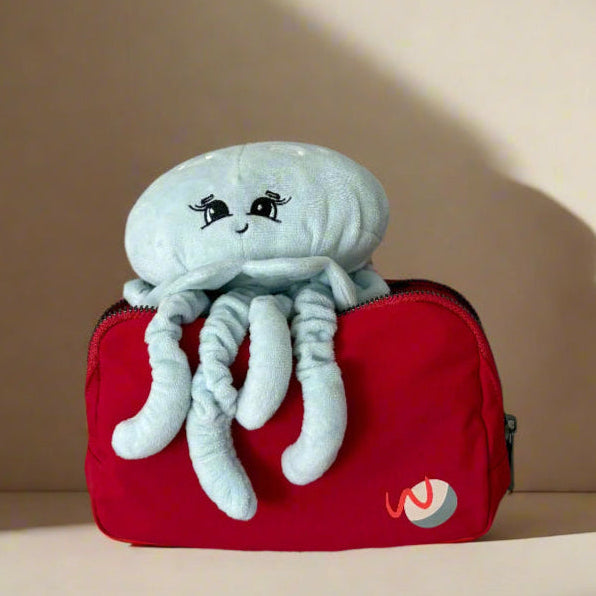 Plush moon jellyfish toy on a red pouch with a logo against a beige background